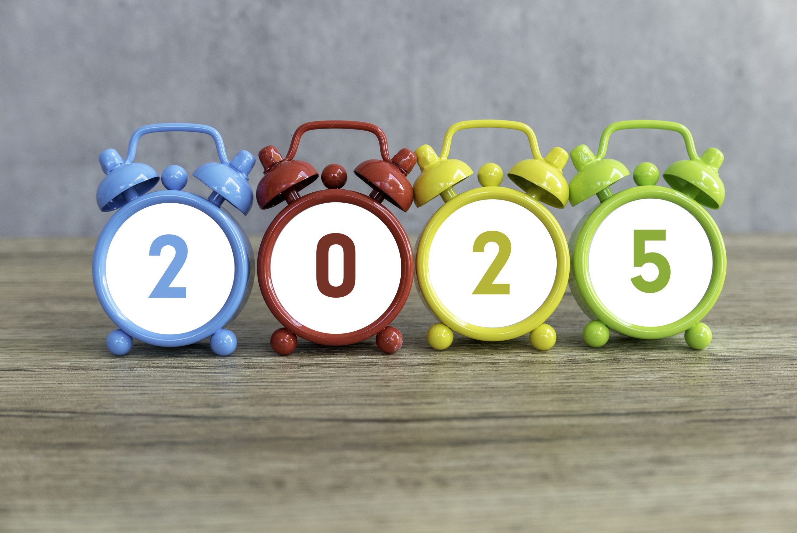 Colorful Alarm Clocks Displaying the New Year 2025 on a Wooden Surface.